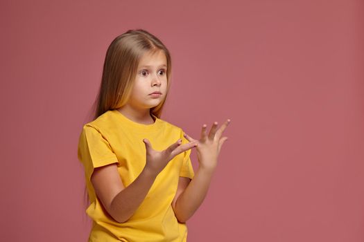 little girl in a yellow t-shirt on coral background. surprised shows hands