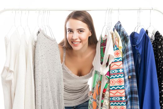 Young beautiful woman smiling at camera while standing between clothes on hanger