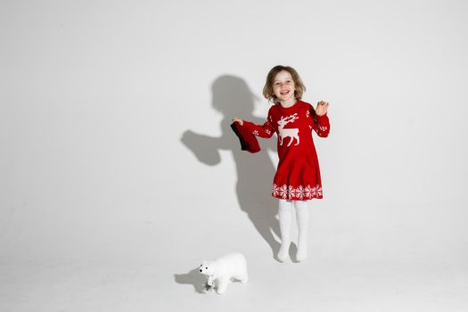 Cheerful little girl on red Christmas dress smiling and jumping for joy beside her toy polar bear. Holiday concept