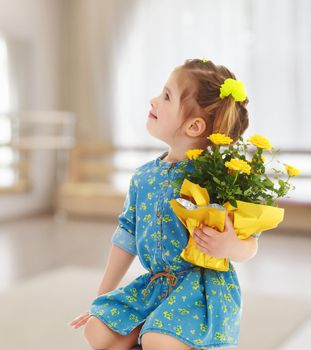 Pensive little girl in a short summer robe, holding a bouquet of yellow flowers.On the background of the hall with a large arched window , the concept of learning and child development.