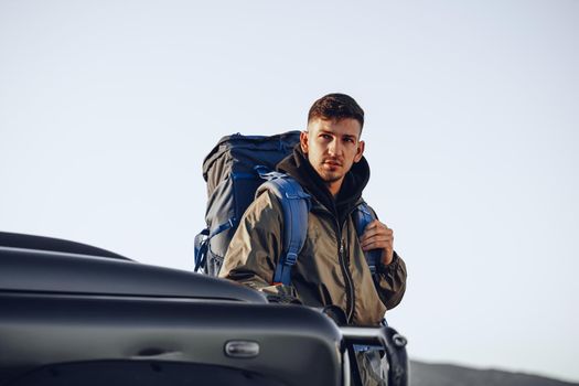 Portrait of a young traveler man in hiking equipment standing near his off-road car at dawn