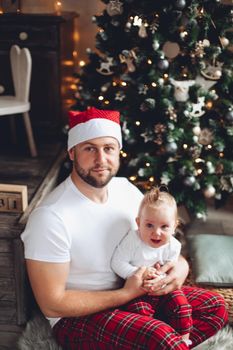 Happy young father holding cute baby with with Christmas tree on the background. Holiday concept