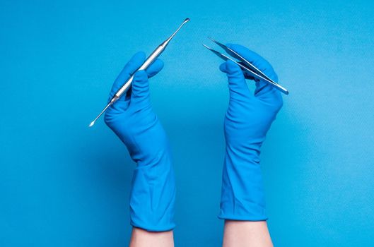 Hands in blue gloves holding dental surgery sticks on light blue background