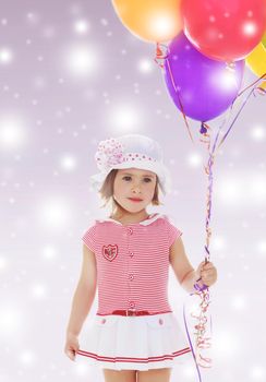 Adorable little girl in short summer dress and white Panama hat on his head. Girl holding bunch of colorful balloons.Close-up.On new year purple background with white snowflakes.