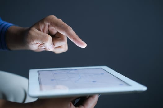 man's hand working on digital tablet at office desk, using self created chart.