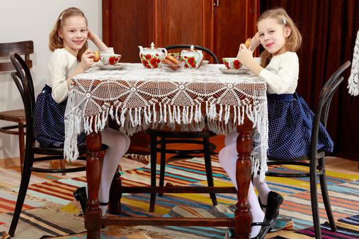 Cute little girls twins drinking tea at an antique table with a lace tablecloth.Retro style.