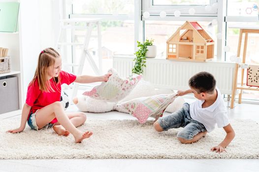 Pretty little boy ang girl fighting pillows in modern playroom