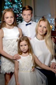 A happy mother with young children on Christmas Eve in a dark room with candles and a fireplace, near a large white grand piano. The concept of a family holiday.