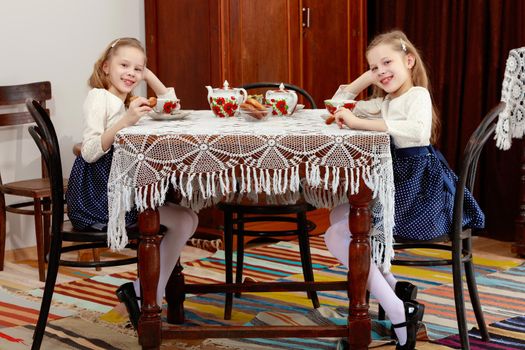 Cute little girls twins drinking tea at an antique table with a lace tablecloth.Retro style.