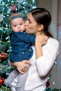 Happy young mother with her little daughter, on Christmas Eve near the Christmas tree with gifts and toys. The concept of holidays and happy childhood.