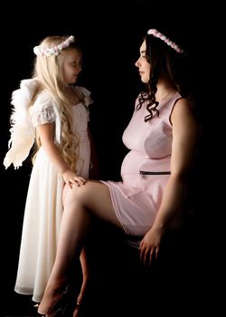 A little girl in the image of an angel hugs the belly of her eldest pregnant sister. The concept of family happiness, the birth of a child.