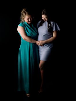 Young pregnant girl with mother on a black background.