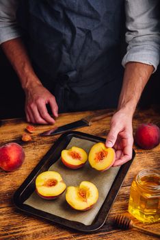 Roast halves of ripe peaches with honey. Chef puts fruits on baking dish