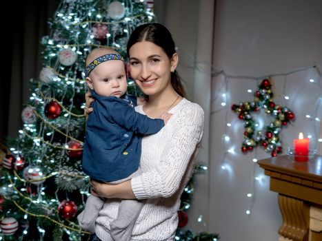 Happy young mother with her little daughter, on Christmas Eve near the Christmas tree with gifts and toys. The concept of holidays and happy childhood.