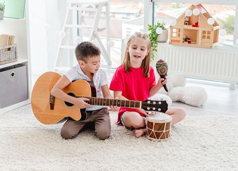 Smiling kids playing on drum and guitar in modern apartment