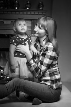 A young mother with a little girl by the fireplace on Christmas Eve. The concept of family happiness, a holiday.