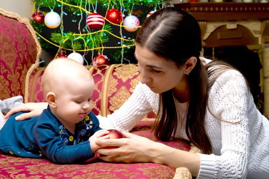 Happy young mother with her little daughter, on Christmas Eve near the Christmas tree with gifts and toys. The concept of holidays and happy childhood.