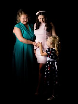 Young pregnant girl with her mother and younger sister on a black background.