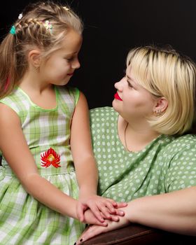 Happy family mom and daughter are hugging on a black background in the studio.