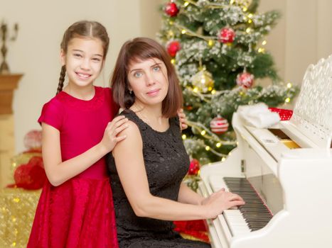 Mom and daughter new years eve near the white piano. Family holidays concept.