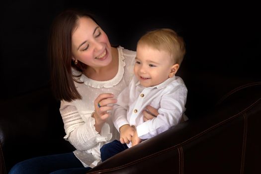 Young mother with a small son in her arms on a black background. The concept of a happy childhood, advertising.