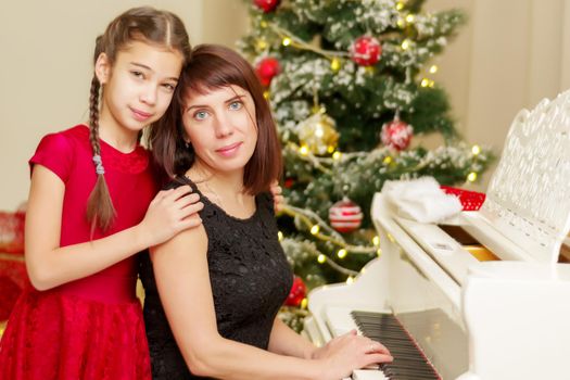 Mom and daughter new years eve near the white piano. Family holidays concept.