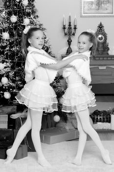 Little twin girls in beautiful white dresses hugging near the fireplace which burn Christmas candles.Black-and-white photo. Retro style.