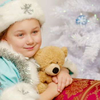 Cute little girl in the costume of the Snow Maiden near the Christmas tree, with a teddy bear. The concept of holidays.