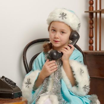 Cute little girl in a snow maiden costume talking on the old phone. The concept of family holidays.