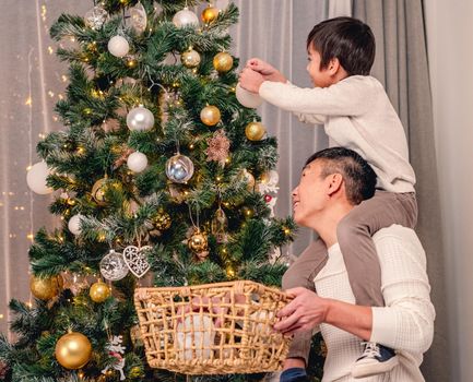 Little son and father putting top star on christmas tree at home