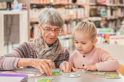 Granddaughter and grandmother put together a puzzle in the library