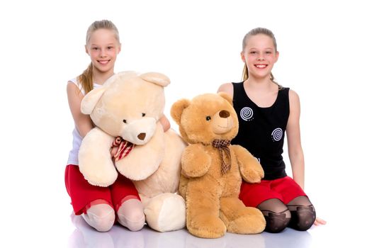 Lovely little girls. Next to a large teddy bear on a white background in the studio. The concept of holidays, happy childhood. Isolated.