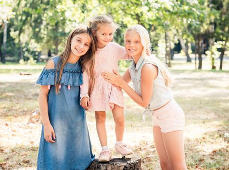 Pretty smiling little girls stand hugging in a sunshine autumn park