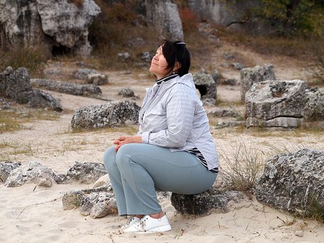 brunette woman meditates sitting on a stone.