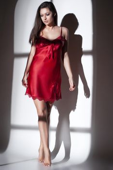 Fashion photo of beautiful woman in red nightdress in light of window