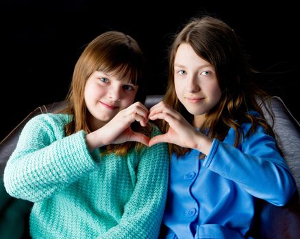 Two school girls folded their hands in the shape of a heart. Concept of friendship, happy people.