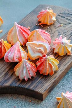 Pink and yellow meringue lies on a wooden board. Nearby are meringue crumbs