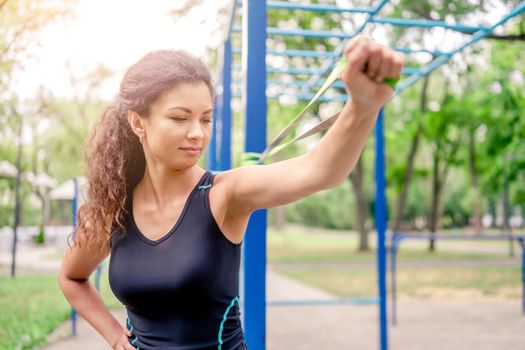 Sport girl with elastic rubber band doing arm workout outdoors. Young woman exercising with fitness equipment at stadium