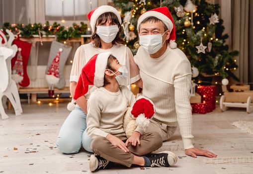 Happy family in protective masks celebrating christmas at home during coronavirus pandemic