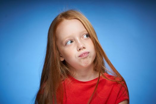 cute red-haired girl in red t-shirt emotions blue background. High quality photo