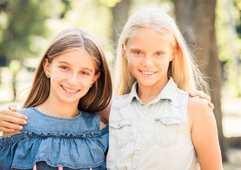 Pretty smiling teenage girls stand hugging in the sunshine park