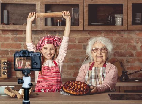 Cheerful grandaughter in chef uniform enjoyed the finished fruit pie with her granny. Blogger profession. Shooting with a camera for a blog