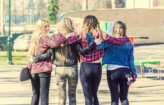 Back view of four girl friends hugging at the skate park. Friendly hugs of best friends. Friendship and unity concept