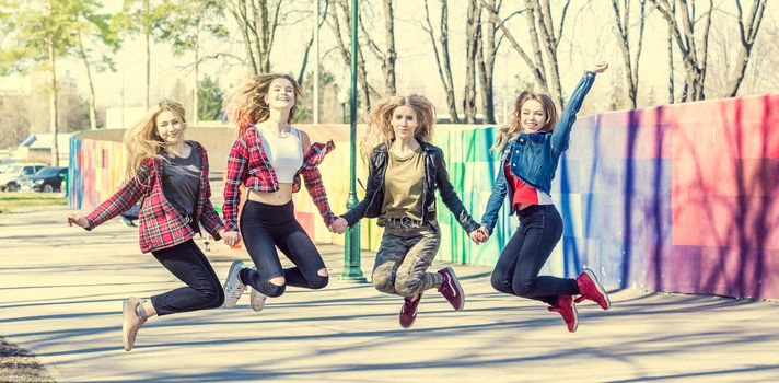 Joyful young girls holding hands and jumping together. Four happy teenage girls friends jumping high at the park. Girls having fun jumping outdoors