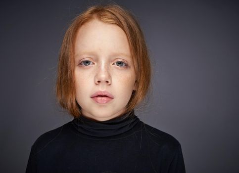 red-haired girl with freckles on her face in a black sweater posing. High quality photo