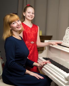 A beautiful young mother with a little daughter near a large white grand piano. The concept of family happiness, music education.