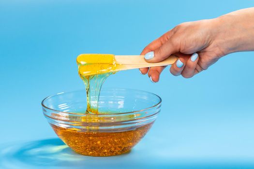 Liquid yellow paste for sugaring on blue background. Hair removal and depilation.