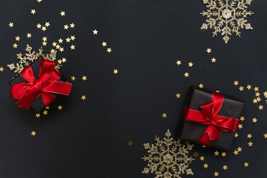 New Year's gifts with red bows on a black background with confetti and gold snowflakes and balls. Preparing for a stylish Christmas party