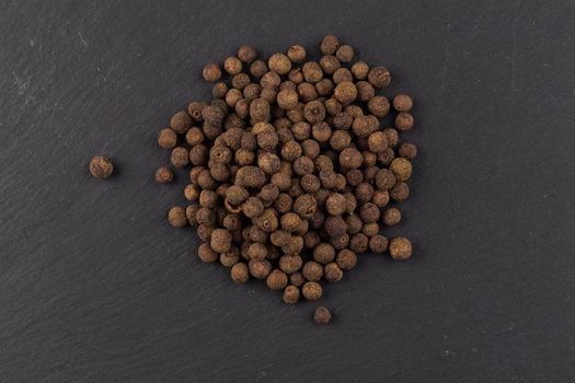 Large black peppercorn seeds on dark stone background