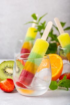 Striped popsicle with different flavors, mango, orange, kiwi and strawberry in glass cups. Summer food concept with copy space.